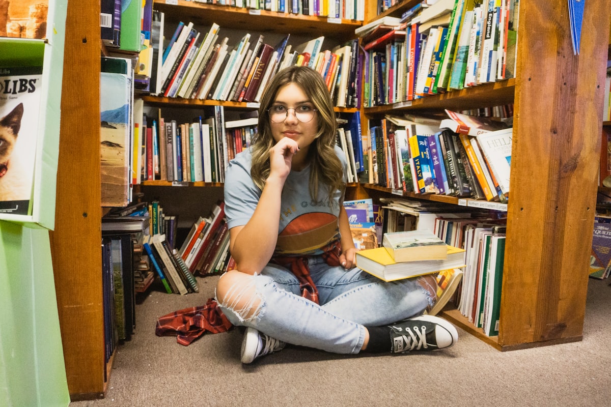 Une adolescente lit, assise devant une bibliothèque